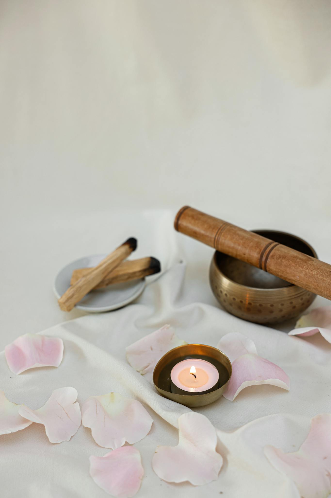 Peaceful arrangement with a Tibetan singing bowl, lighted candle, and rose petals for meditation and relaxation.